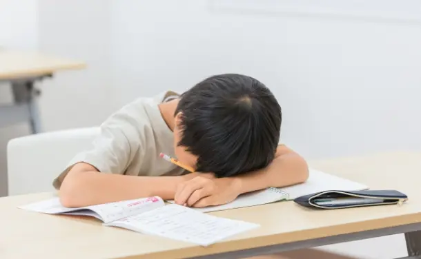 若い男の子が机で眠っている様子。周りは静かな雰囲気です。